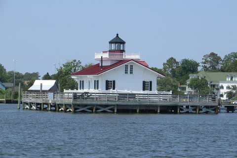 A white cottage-style lighthouse on a pier over the water at the Manteo waterfront