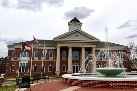 Brick town hall with white columns and a cupola behind a splashing fountain in Mint Hill