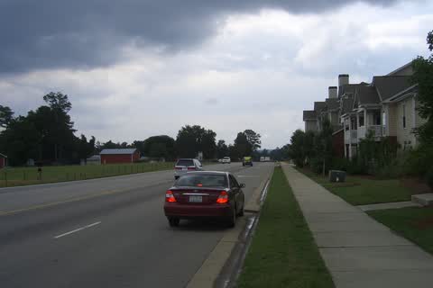 A two-lane road with apartments on one side and open fields on the other in Morrisville
