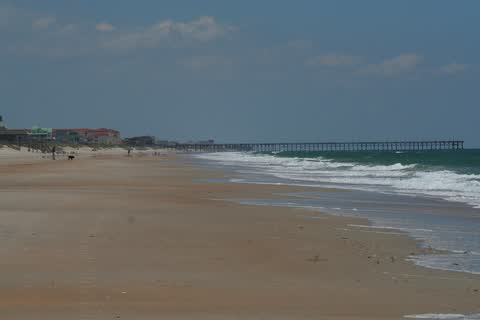 A wide sandy beach with a fishing pier in the distance at North Topsail Beach