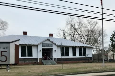 A long one-story white school building beside the road in Princeville