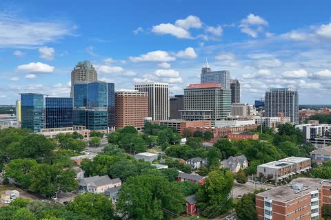 Downtown Raleigh's office towers rising above a tree canopy under a blue sky