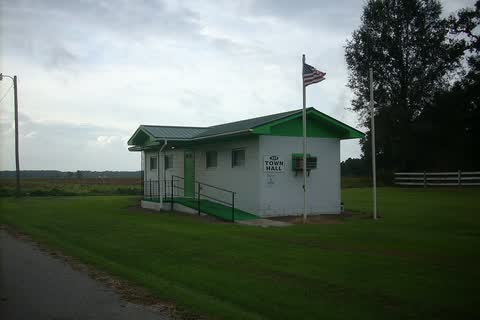 Raynham Town Hall, a small green-and-white building with a flagpole beside a gravel drive