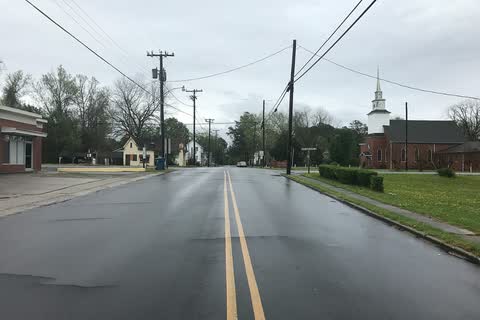 A two-lane road through Roper with a white church steeple in the distance