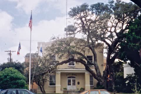 A historic building with a flagpole under large live oaks in Southport