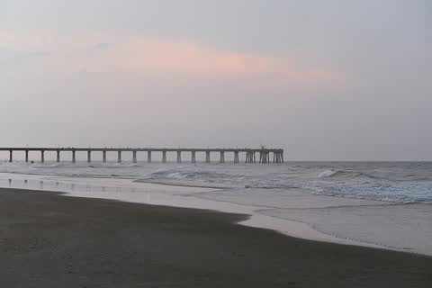 A wide sandy beach at dusk in Surf City with the long Surf City Pier stretching out over the ocean