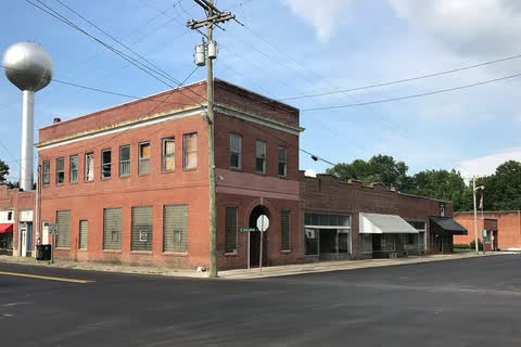 A two-story brick commercial building at a corner with the water tower behind in Walstonburg