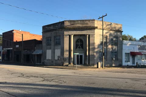 A small classical bank-style building and storefronts at a corner in Whitakers