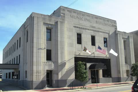 A pale stone Art Deco municipal building with flags at the entrance in Wilson