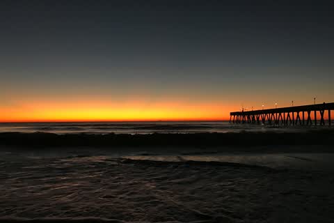 The ocean at sunrise off Wrightsville Beach, an orange band on the horizon and a long fishing pier reaching out from the beach