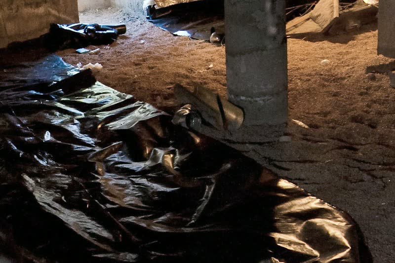 Black plastic sheeting, a ground vapor barrier, laid over part of the dirt floor of a crawl space, beside a concrete pier.